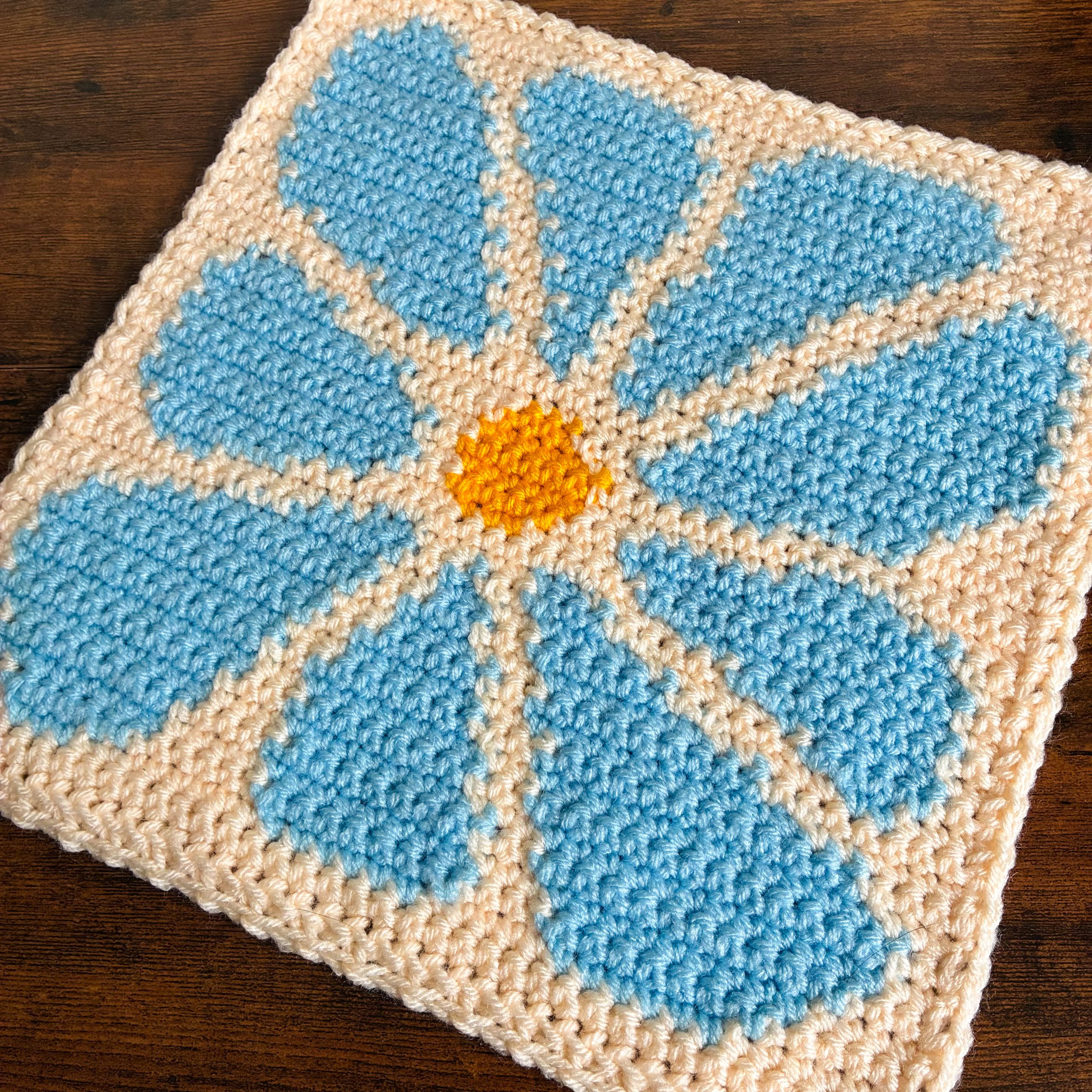 Petal-and-patch-flatlay-square-2 Crochet flower square from the Petal & Patch Blanket beside yarn skeins, showing the finished floral motif and coordinating color palette.